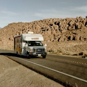 RV driving through a scenic desert highway with rocky mountains under a clear sky.