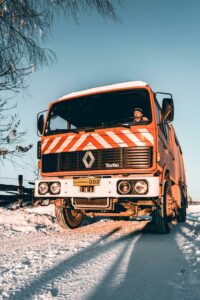 Red truck navigating a snowy road during winter with clear blue sky.