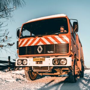 Red truck navigating a snowy road during winter with clear blue sky.