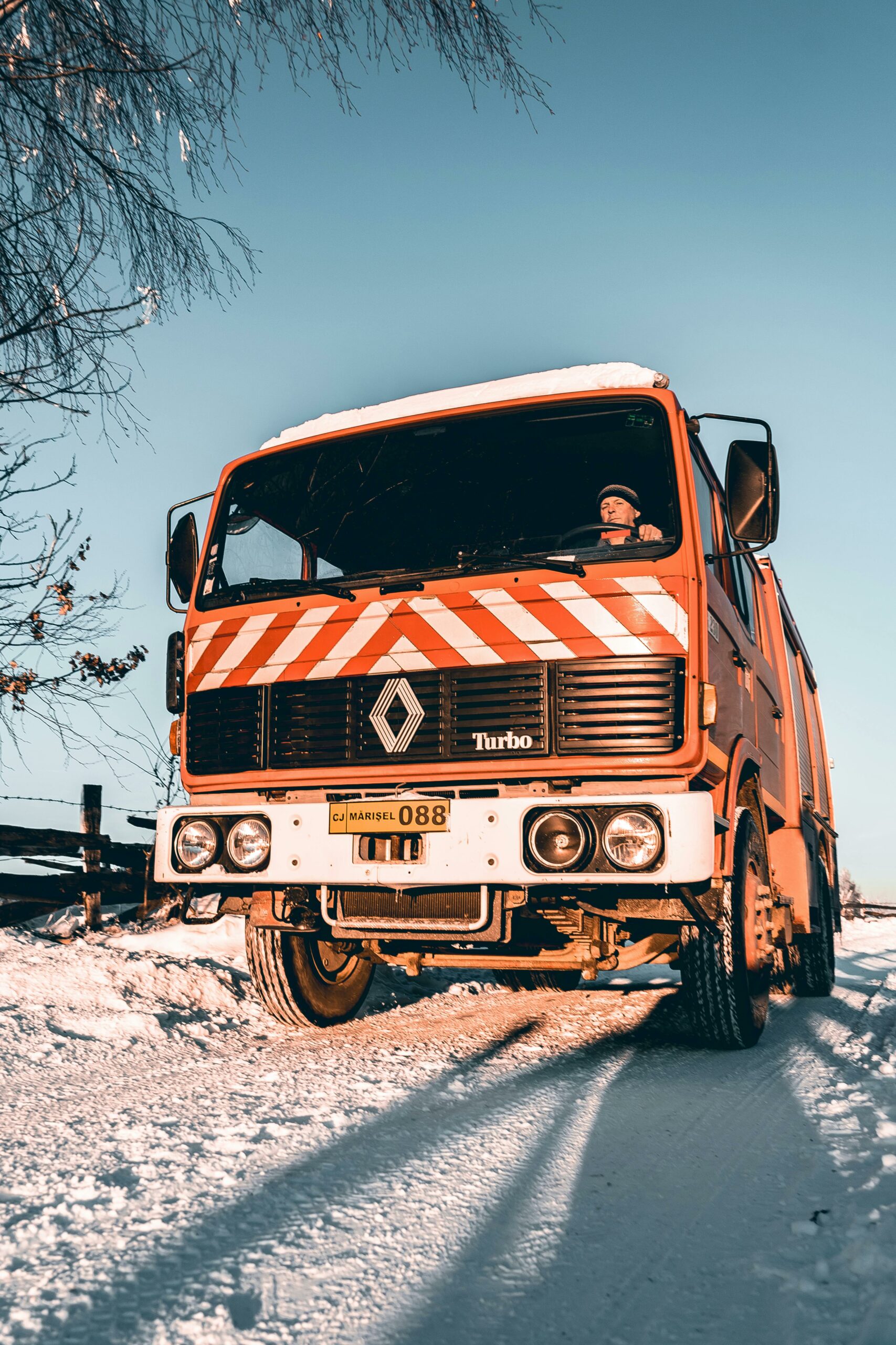 Red truck navigating a snowy road during winter with clear blue sky.